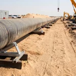 Lange Pipeline-Strecke auf Rohrrollen-Bockstationen während der Verlegearbeiten in sandigem Gelände mit Mobilkran im Hintergrund.