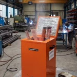 Ein orangefarbener Elektroden-Trockenofen von Küppersbusch im Einsatz in einer Fertigungshalle, befüllt mit Stabelektroden zur Vorwärmung für anstehende Schweißarbeiten.