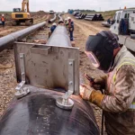 Ein Schweißer führt Präzisionsarbeiten an einer Pipeline durch, während ein magnetisches Hitzeschutzschild ihn und die Umgebung vor Funkenflug und extremer Hitze schützt.