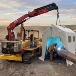 Schweißraupe im Außeneinsatz mit einem Schweißzelt, das einen Facharbeiter beim Schweißen einer Pipeline vor Witterungseinflüssen schützt.