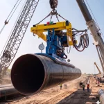 Vakuumheber am Kran transportiert ein schweres Stahlrohr sicher über eine Pipeline-Baustelle im Außenbereich.