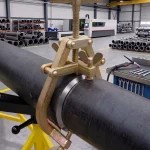 Mechanische Schnellspann-Außenzentrierklemme im Einsatz zur präzisen Fixierung zweier Rohrsegmente vor dem Schweißvorgang in einer Industriehalle.